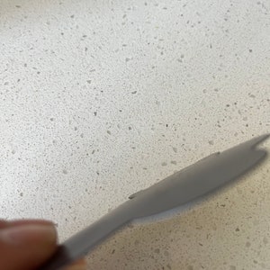 May include: A close-up of a gray silicone spatula on a white countertop with flecks of gray.