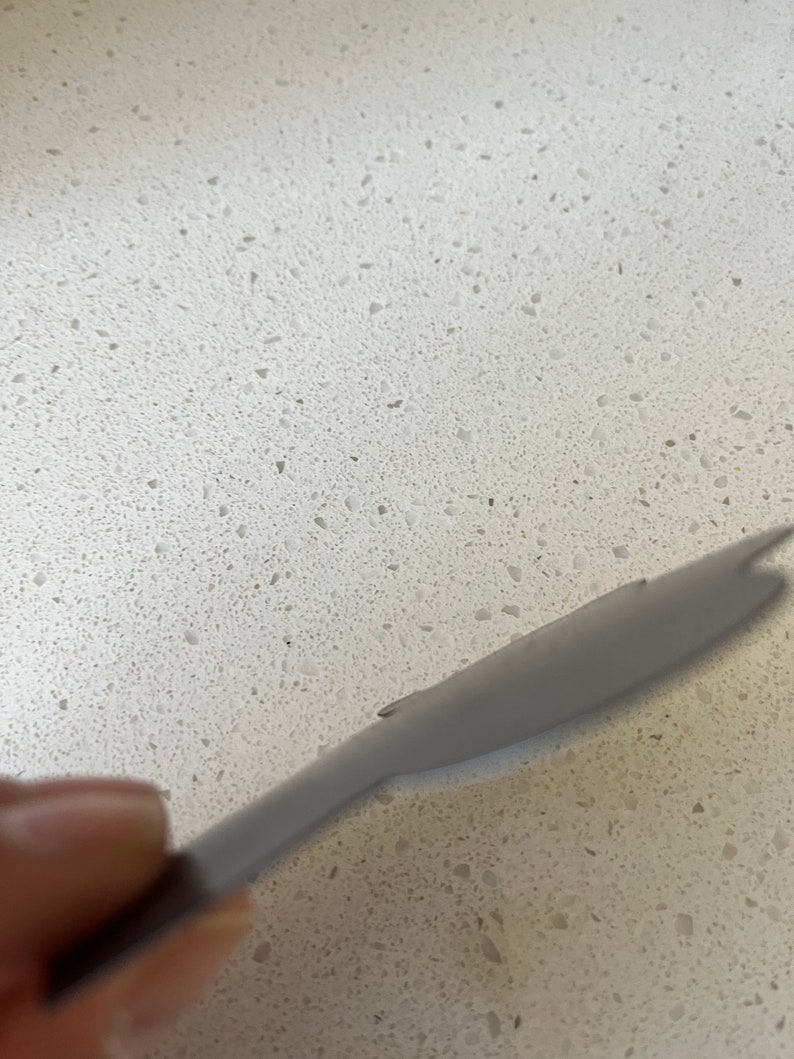 May include: A close-up of a gray silicone spatula on a white countertop with flecks of gray.