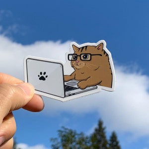May include: A brown cat wearing glasses is sitting at a laptop computer. The cat has a paw print on the laptop.