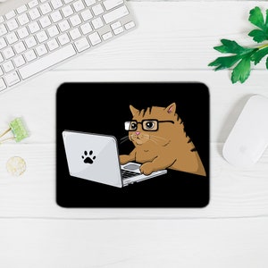 May include: A black mouse mat featuring a cartoon illustration of a brown cat wearing glasses and using a laptop computer. The cat has a paw print on its laptop.