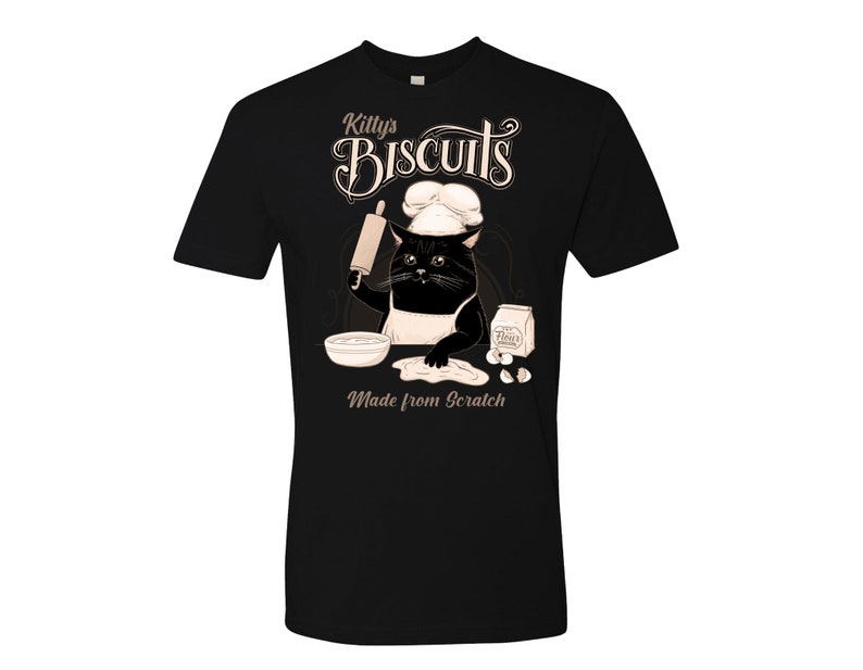 May include: Black t-shirt with a graphic of a cat wearing a chef's hat and holding a rolling pin. The text "Kitty's Biscuits Made from Scratch" is printed on the shirt.