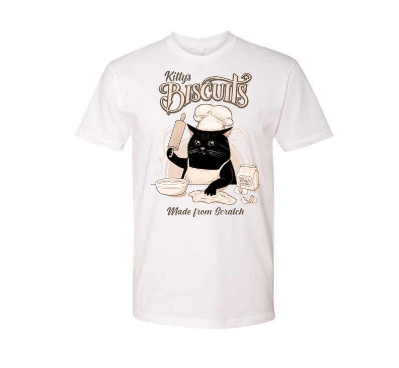 May include: White t-shirt with a black cat wearing a chef's hat and holding a rolling pin. The cat is making biscuits, with the text "Killy's Biscuits Made from Scratch" on the shirt.