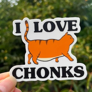 May include: White sticker with a cartoon orange tabby cat with black stripes. The cat is walking and has a large belly. The text "I LOVE CHONKS" is printed in black on the sticker.