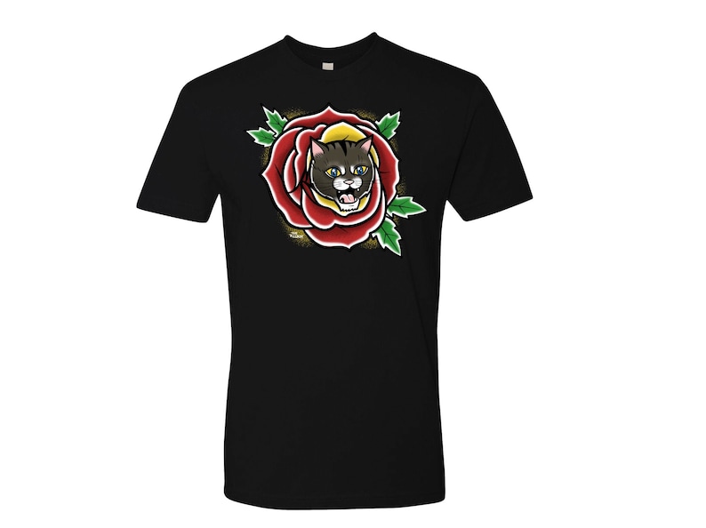 May include: Black t-shirt featuring a colorful graphic of a cat's face inside a red rose. The cat has yellow eyes and is surrounded by green leaves. The design is reminiscent of traditional tattoo art.