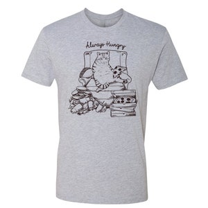 May include: A gray t-shirt with a black and white illustration of a cat sitting in a chair surrounded by pizza boxes and food. The text "Always Hungry" is printed on the shirt.