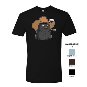 May include: Black cat wearing a brown cowboy hat with the word "MEOWDY" above it. The cat is looking to the right and has a small piece of straw in its mouth. The cat is on a black t-shirt.