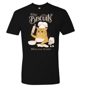 May include: Black t-shirt with a cartoon cat wearing a chef's hat and holding a rolling pin. The cat is making biscuits, with the text "Kitty's Biscuits Made from Scratch" on the shirt.