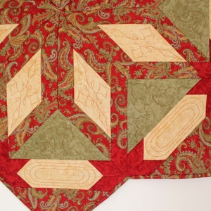 Puede incluir: Primer plano de un textil acolchado con un estampado de cachemira rojo, acentuado por formas geom&eacute;tricas beige y verdes. El dise&ntilde;o presenta elementos de diamante y rectangulares con costuras decorativas.