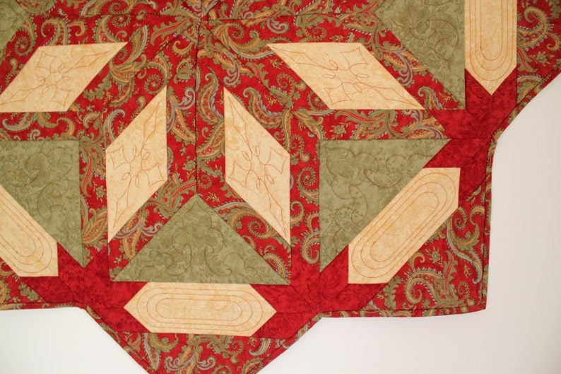 Puede incluir: Primer plano de un textil acolchado con un estampado de cachemira rojo, acentuado por formas geom&eacute;tricas beige y verdes. El dise&ntilde;o presenta elementos de diamante y rectangulares con costuras decorativas.
