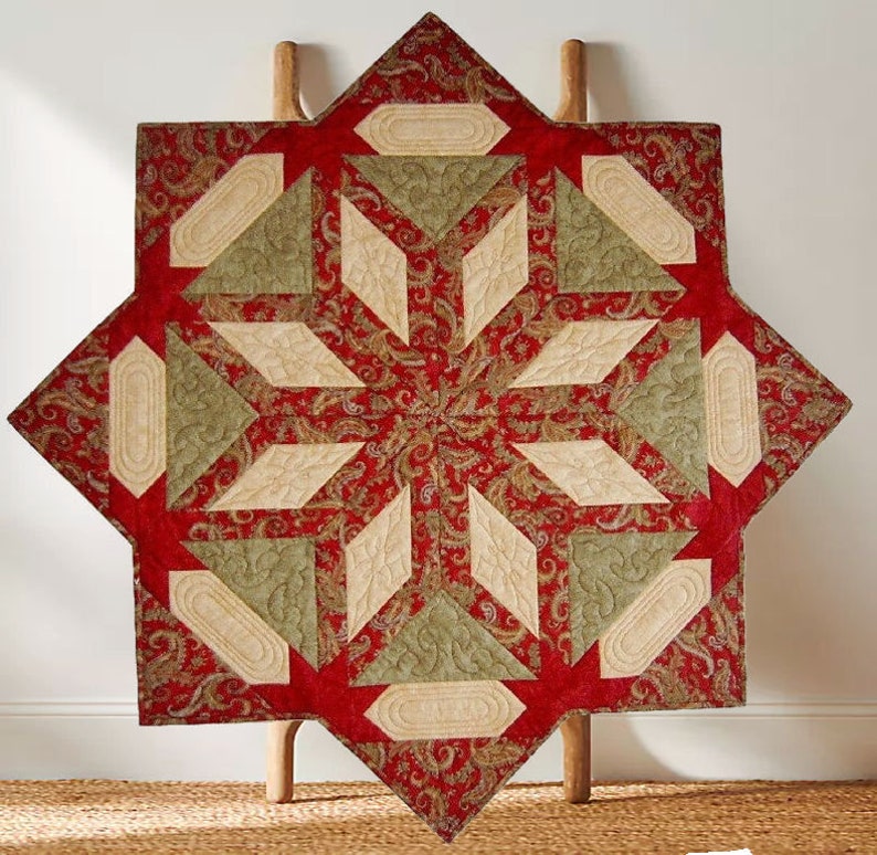 Puede incluir: Un mantel individual acolchado en forma de estrella con un estampado de cachemira rojo. El dise&ntilde;o incluye formas geom&eacute;tricas beige y verde oliva. El mantel se exhibe sobre una escalera de madera, mostrando su atractivo decorativo.