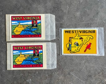 Könnte beinhalten: Drei Vintage-Souvenir-Aufkleber aus West Virginia. Die Aufkleber zeigen eine Karte des Bundesstaates mit verschiedenen Städten und Sehenswürdigkeiten, die beschriftet sind. Die Aufkleber sind gelb, rot und blau auf weißem Hintergrund.