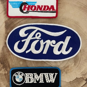 May include: Three embroidered patches featuring automotive brand logos. The top patch is rectangular with "HONDA" in red, a black gear, and blue accents. The middle patch is oval with "FORD" in white on a blue background. The bottom patch is black with "BMW" in white and a blue and white logo.