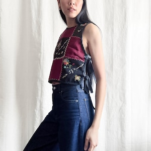 May include: A sleeveless patchwork top with embroidered floral details and a burgundy and black color scheme. The top is paired with dark wash denim jeans. The text "W.B. THAMM FRANKLY MADE IN NYC" is visible.