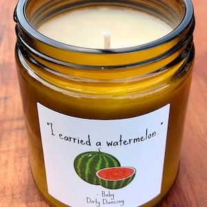 May include: A brown glass candle jar with a white label. The label has a green and red watermelon illustration and the text "I carried a watermelon." - Baby Dirty Dancing.