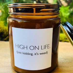 May include: A brown glass jar candle with a white label that reads "HIGH ON LIFE. (just kidding, it's weed)"