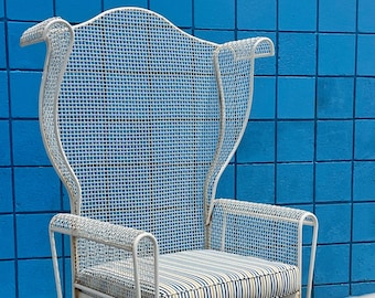 May include: White metal outdoor chair with a high back and armrests. The chair features a wire mesh design and a striped cushion in blue, tan, and white. The chair is set against a blue tiled wall.