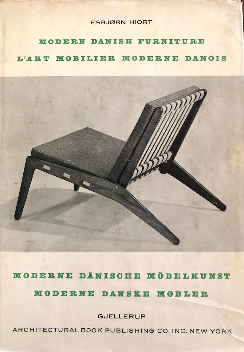 Puede incluir: Una fotograf&iacute;a en blanco y negro de una silla de madera con respaldo tejido y asiento de tela gris. La silla est&aacute; inclinada hacia la derecha y el respaldo de la silla est&aacute; orientado hacia el espectador. La silla est&aacute; sobre un fondo blanco. El texto "MODERN DANISH FURNITURE" est&aacute; en la parte superior de la imagen. El texto "L'ART MOBILIER MODERNE DANOIS" est&aacute; debajo de la primera l&iacute;nea de texto. El texto "MODERNE D&Auml;NISCHE M&Ouml;BELKUNST" est&aacute; en la parte inferior de la imagen. El texto "MODERNE DANSKE M&Oslash;BLER" est&aacute; debajo de la l&iacute;nea de texto anterior. El texto "GJELLERUP" est&aacute; debajo de la l&iacute;nea de texto anterior. El texto "ARCHITECTURAL BOOK PUBLISHING CO. INC. NEW YORK" est&aacute; debajo de la l&iacute;nea de texto anterior.