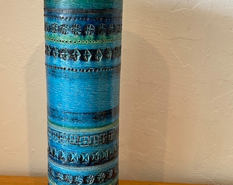 May include: A tall, cylindrical blue ceramic vase with a geometric pattern. The vase has a wide base and a narrow neck.