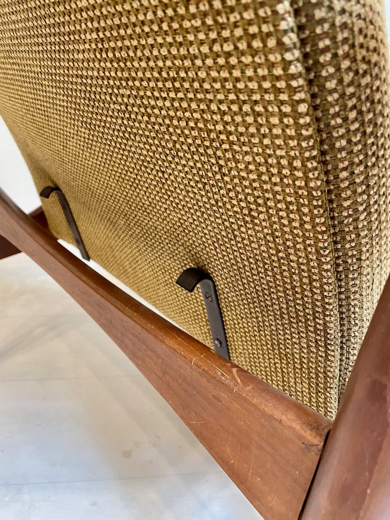 May include: Close-up of a mid-century modern chair. The chair features a wooden frame with a warm brown finish and a woven fabric seat and backrest in shades of olive green and brown. The chair has a minimalist design.