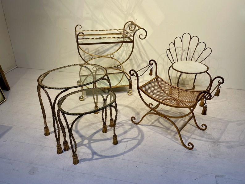 Puede incluir: Una colecci&oacute;n de muebles vintage de metal dorado. Incluye dos mesas nido con tapas de cristal y patas en forma de cuerda, un carrito de servicio, un banco con asiento tejido y una silla en forma de concha.
