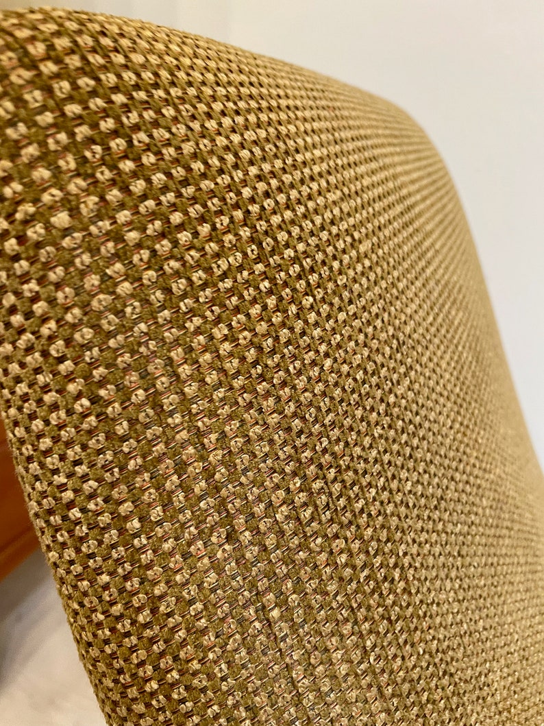 May include: Close-up of a chair back with a textured, woven fabric. The fabric has a repeating pattern of small, square-like shapes in shades of tan, brown, and a hint of red. The overall appearance is neutral and warm.