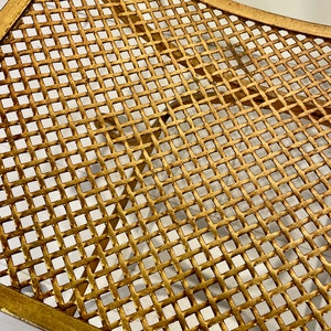 Puede incluir: Primer plano de una mesa decorativa de metal dorado con dise&ntilde;o de celos&iacute;a. La mesa tiene una forma curva y un patr&oacute;n de rejilla. El metal tiene un acabado ligeramente envejecido, lo que aumenta su atractivo vintage.