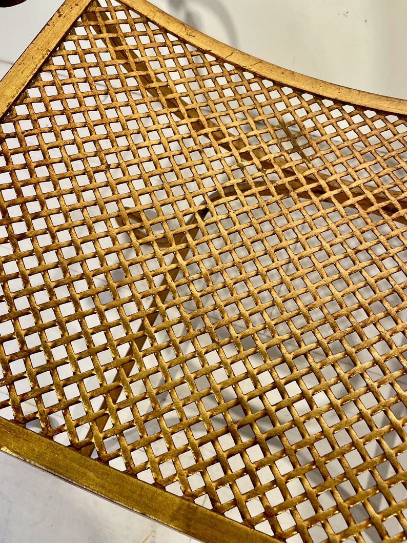 Puede incluir: Primer plano de una mesa decorativa de metal dorado con dise&ntilde;o de celos&iacute;a. La mesa tiene una forma curva y un patr&oacute;n de rejilla. El metal tiene un acabado ligeramente envejecido, lo que aumenta su atractivo vintage.
