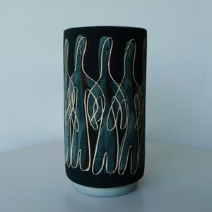 May include: A black ceramic vase with a white and brown abstract design. The design features a repeating pattern of stylized figures.