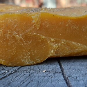 May include: A large, irregular chunk of beeswax, with a rough, textured surface. The beeswax is a deep yellow color.
