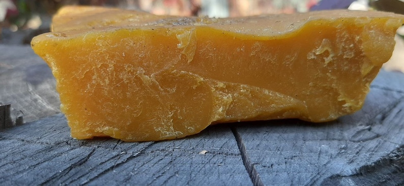 May include: A large, irregular chunk of beeswax, with a rough, textured surface. The beeswax is a deep yellow color.