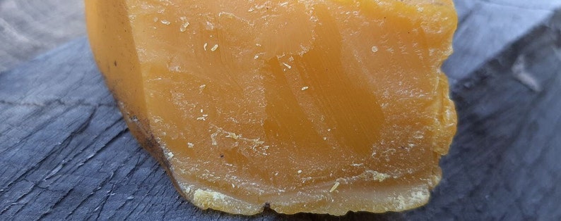 May include: A large block of yellow beeswax. The beeswax has a rough, textured surface.