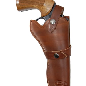 May include: A brown leather holster with a snap closure and a belt loop. The holster is designed to hold a revolver. The holster has a logo that says "Frontier Leather Goods Co."