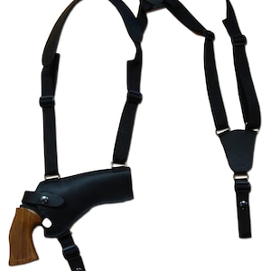 Może przedstawiać: Czarna skórzana kabura na ramię z rewolwerem z drewnianą rękojeścią. Kabura ma regulowane czarne paski i element łączący z tyłu. Rewolwer ma brązowy drewniany uchwyt.