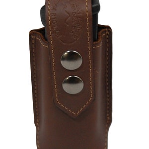 Może przedstawiać: Brązowa skórzana kabura na magazynek z dwoma srebrnymi zatrzaskami i wytłoczonym tekstem "Genuine Leather Handcrafted in the USA" z przodu.