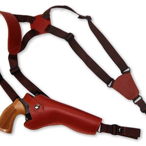 May include: A brown leather holster with a shoulder strap for carrying a handgun. The holster has a flap that covers the gun and a strap that goes over the shoulder.