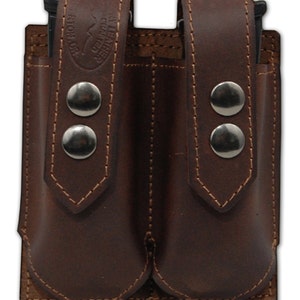 Może przedstawiać: Podwójna kabura na magazynki wykonana ze skóry brązowej z srebrnymi nitami i przeszyciami. Kabura ma dwa oddzielne przedziały na magazynki.