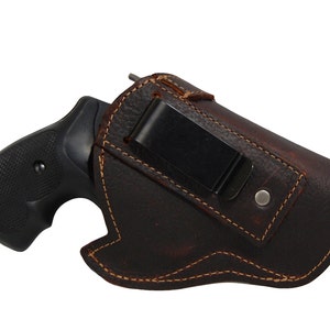 Könnte beinhalten: Ein braunes Lederholster mit einem Metallclip für eine Pistole. Das Holster hat einen genähten Rand und einen Used-Look.