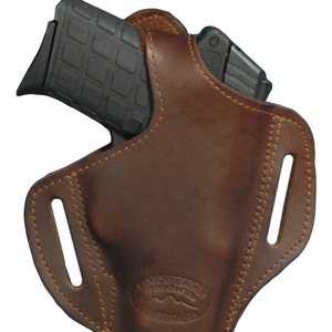 K&ouml;nnte beinhalten: Ein braunes Lederholster f&uuml;r eine Pistole mit einem G&uuml;rtelclip und dem Text "Varsity Leather Handcrafted" in einem Kreis.