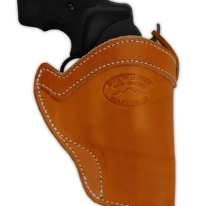 Op de afbeelding: Een bruine leren holster met witte stiksels voor een revolver. De holster heeft een merkteken van de maker met de tekst "Barsony Leather, Hand Crafted, Beaverton, OR".