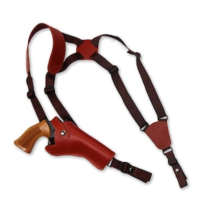 Może przedstawiać: Brązowa skórzana kabura na ramię z pasującym brązowym rewolwerem. Kabura jest przeznaczona do noszenia pod ramieniem i ma regulowane paski. Rewolwer ma drewniany uchwyt.