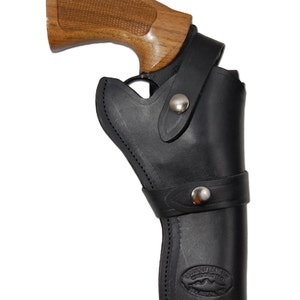 Może przedstawiać: Czarna skórzana kabura z srebrnym zapięciem na zatrzask, trzymająca rewolwer z drewnianym uchwytem. Kabura ma szyty wzór i logo na dole. Uchwyt rewolweru jest w kolorze jasnobrązowym.