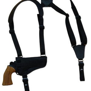 Może przedstawiać: Czarny taktyczny holster na ramię z regulowanymi paskami i skórzaną podkładką. Holster jest przeznaczony do przenoszenia broni palnej.