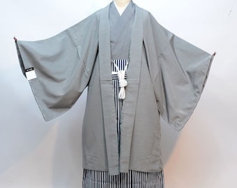 Puede incluir: Un haori gris, una túnica exterior tradicional japonesa, con una faja blanca y un hakama a rayas blancas y negras, una falda tradicional japonesa.