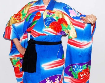 May include: A blue silk kimono with a colourful floral pattern and gold accents. The kimono has a black sash and is being worn.