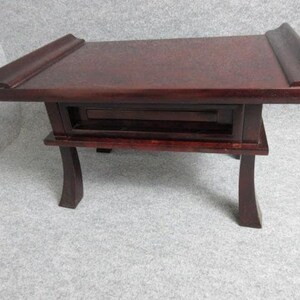 Può includere: Tavolino in legno rosso scuro con piano rettangolare e cassetto. Il tavolo ha gambe curve e un bordo decorativo sulla parte superiore. Misura circa 61 cm di lunghezza, 30 cm di larghezza e 25 cm di altezza.