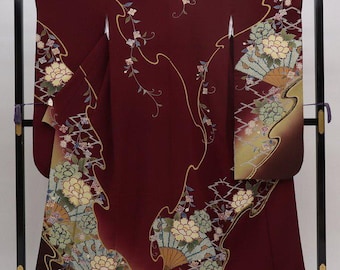 May include: A burgundy kimono with a gold and green floral pattern. The kimono is displayed on a black stand.