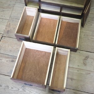 May include: Open wooden cabinet with multiple drawers. The drawers are empty and made of light brown wood. The cabinet is made of dark brown wood.