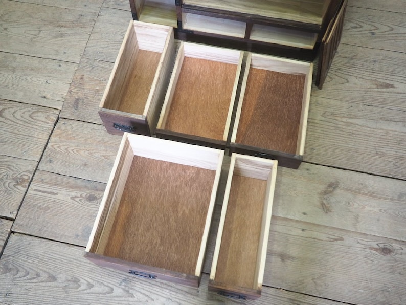May include: Open wooden cabinet with multiple drawers. The drawers are empty and made of light brown wood. The cabinet is made of dark brown wood.