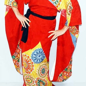 May include: A red kimono with a colourful floral pattern. The kimono has a black sash and long sleeves.