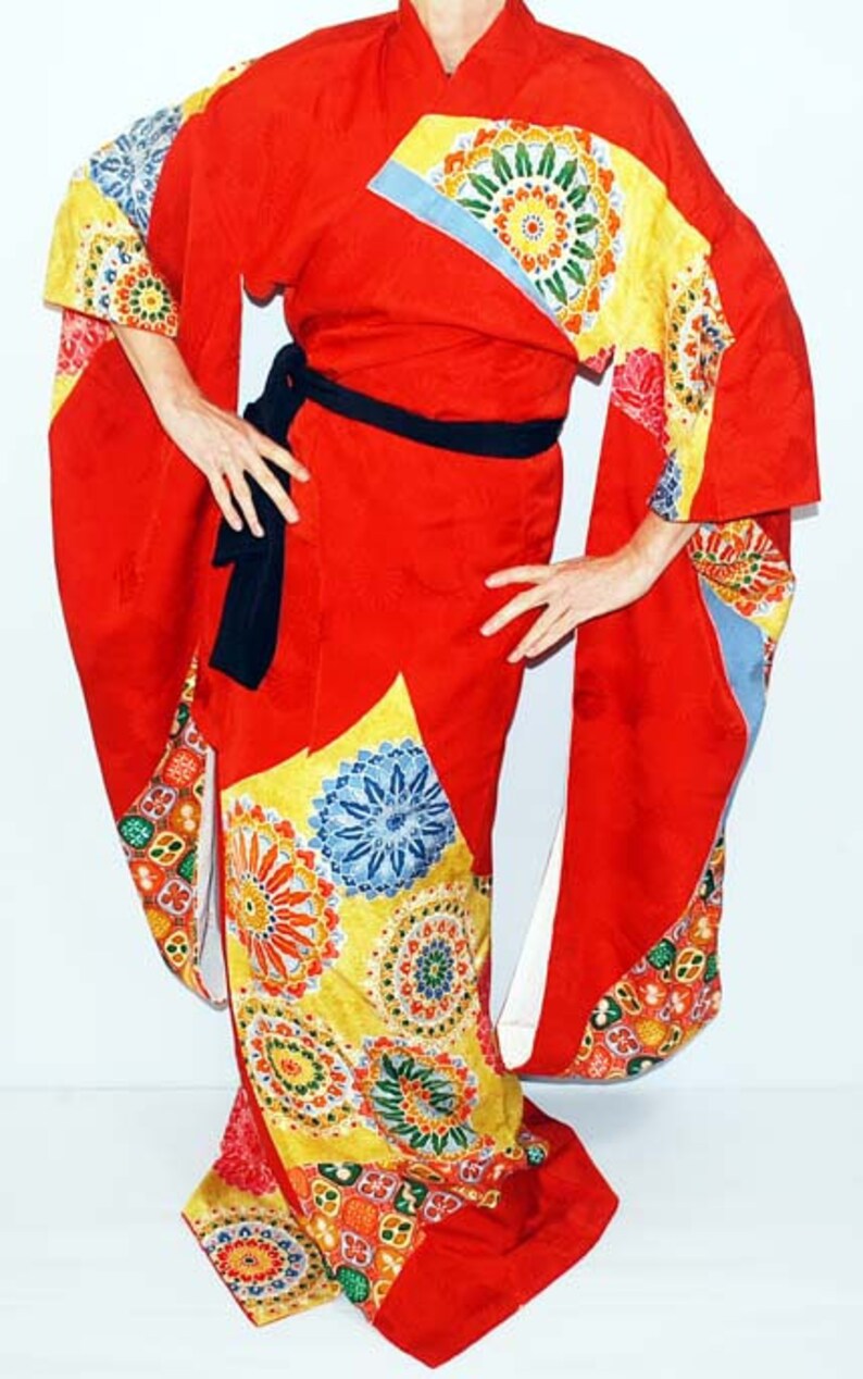 May include: A red kimono with a colourful floral pattern. The kimono has a black sash and long sleeves.